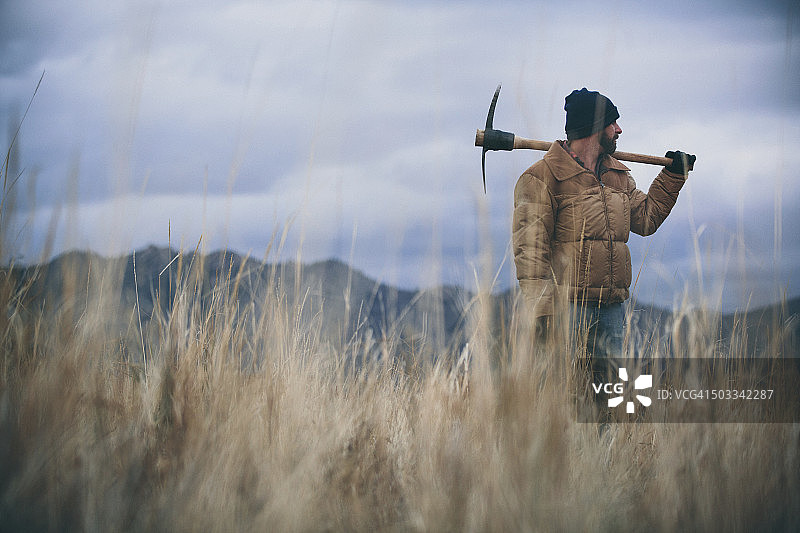 男人在黄昏时分扛着鹤嘴锄站在干草田中图片素材