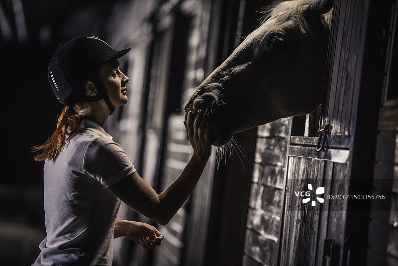 女人晚上在马厩里喂马图片素材