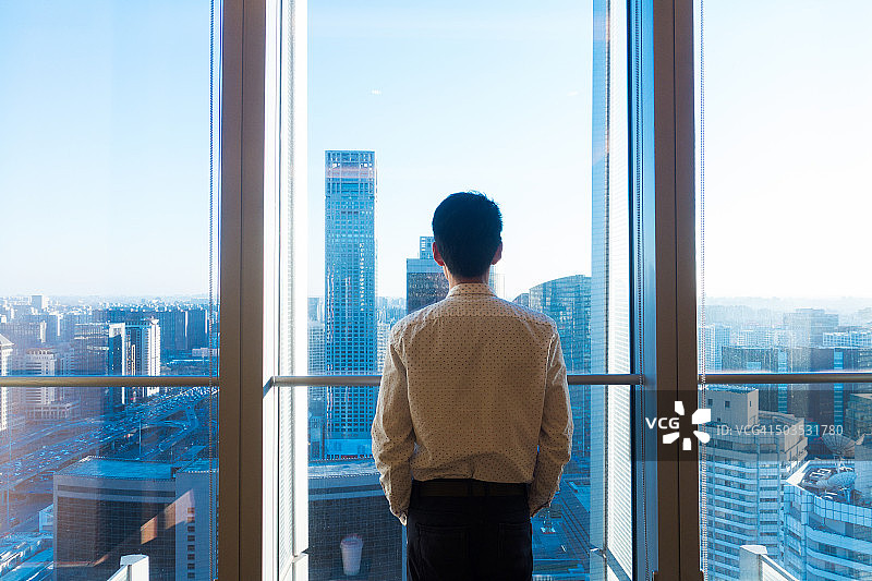 透过办公室窗户查看城市景观的商人图片素材