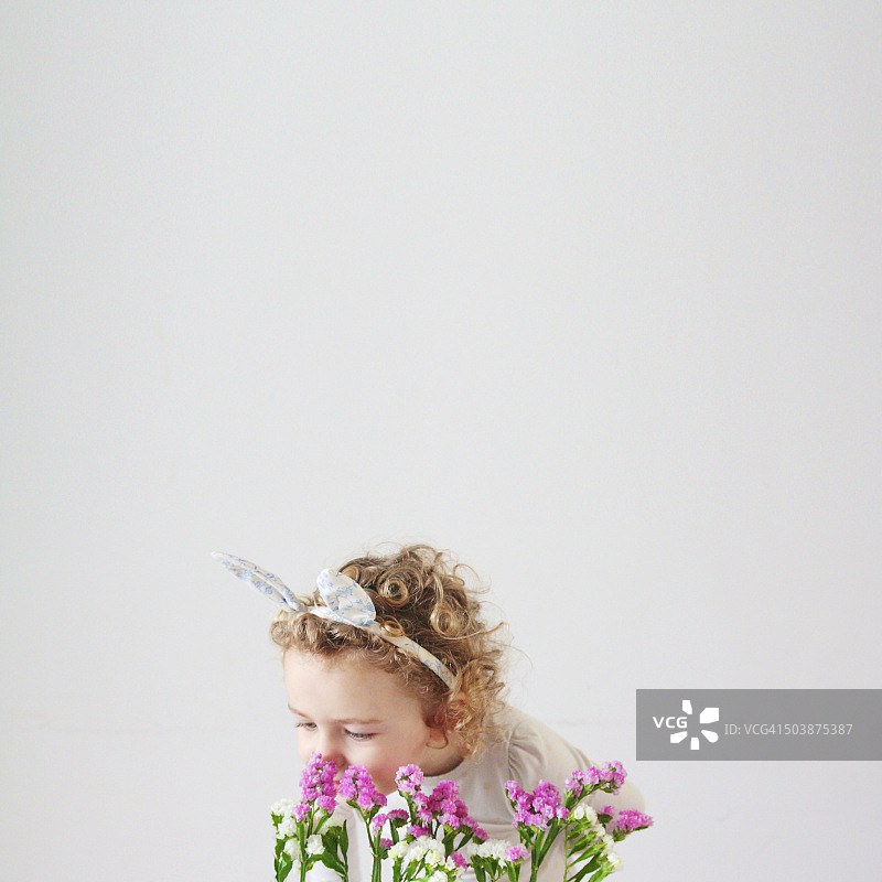 戴着兔子耳朵闻花的少女（2-3岁）图片素材