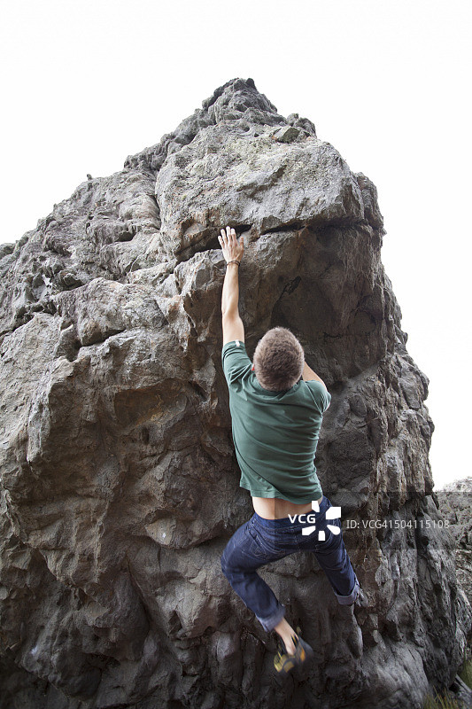年轻男人在新西兰Wainuiomata海岸抱石攀岩图片素材