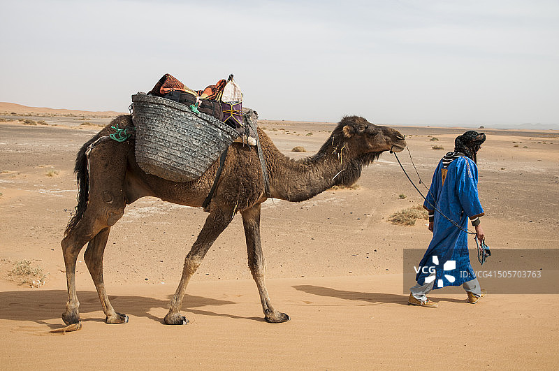 骑着骆驼的年轻骆驼司机在 Erg Chebbi 沙漠图片素材