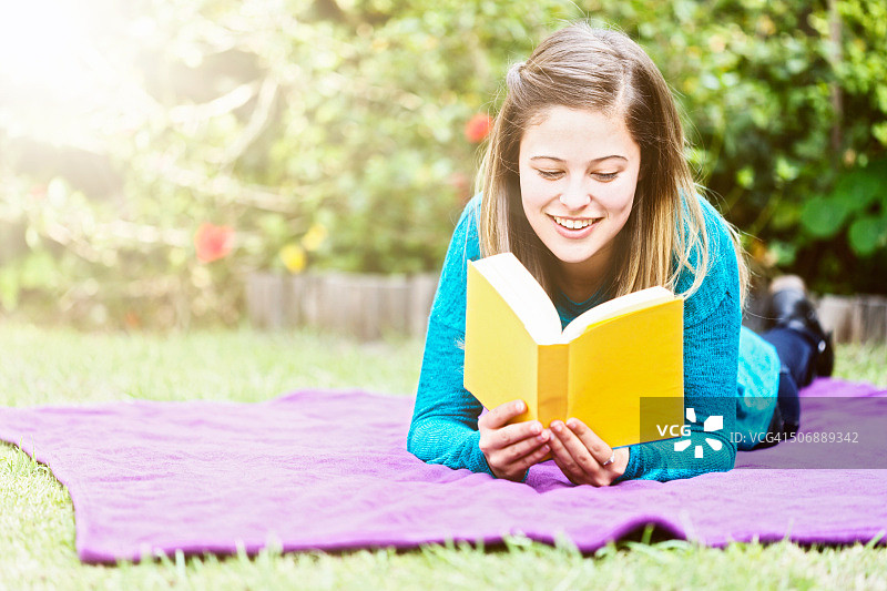 少女在花园里阅读纸质书并微笑图片素材