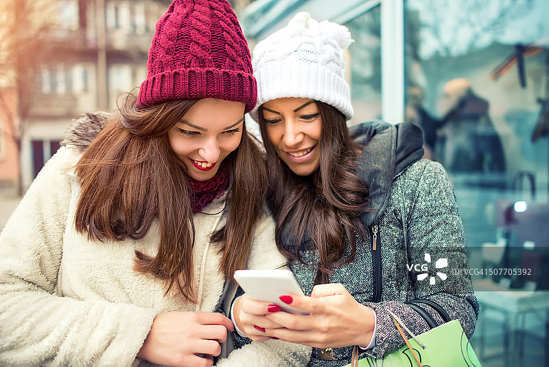 朋友们拿着购物袋在街上使用智能手机图片素材