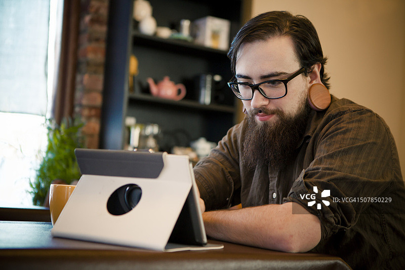 在咖啡馆里喝咖啡和使用平板电脑的年轻男人图片素材