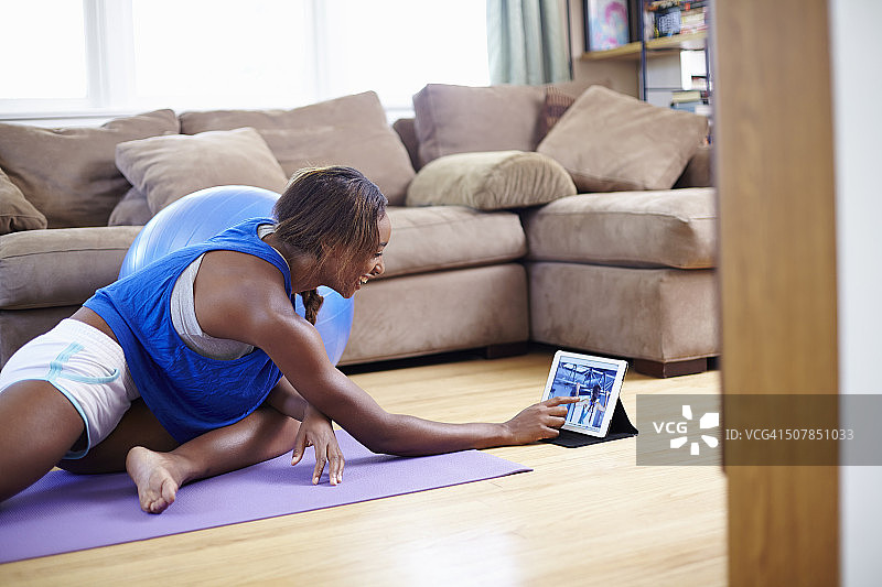 年轻女人在客厅地板上使用触摸屏平板电脑锻炼图片素材