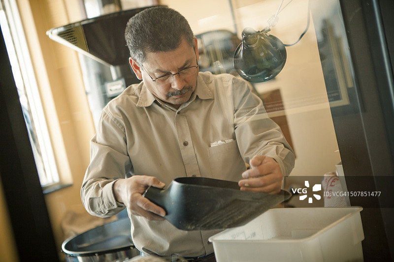 年长的男人在咖啡馆中使用咖啡豆勺为咖啡烘焙机服务图片素材