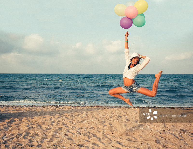 在海滩上跳跃的拿着一束气球的女孩图片素材