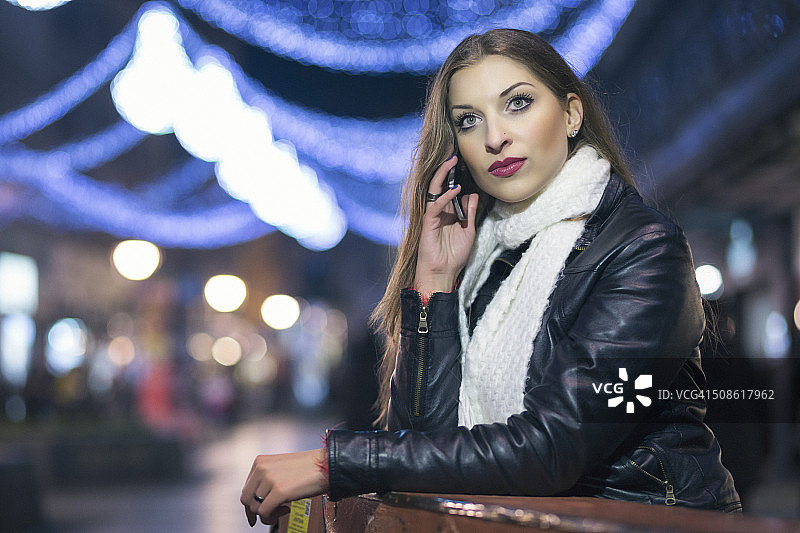 夜晚城市中玩手机的女孩图片素材