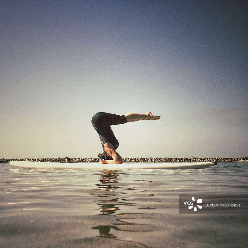 女人在美国加利福尼亚桨板上辅助瑜伽倒立图片素材