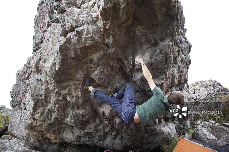 年轻男人在新西兰Wainuiomata海岸抱石攀岩图片素材