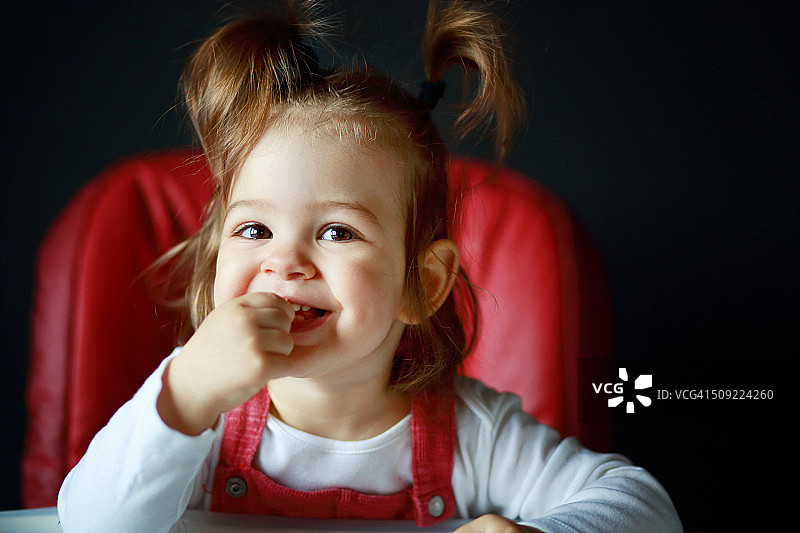 坐在椅子上，手放在嘴里的可爱微笑女婴图片素材