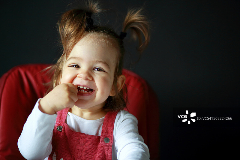 坐在椅子上，手放在嘴里的可爱微笑女婴图片素材