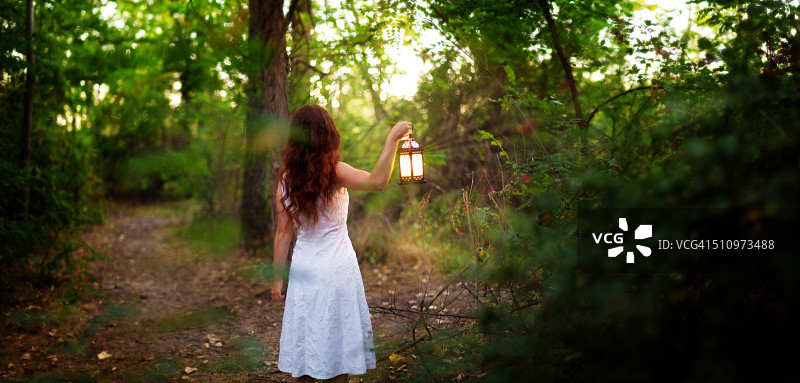红发女子在森林小路上提着灯笼的背影图片素材