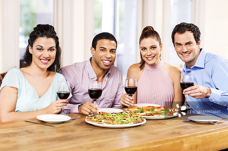 朋友们在餐桌旁享用披萨和葡萄酒图片素材