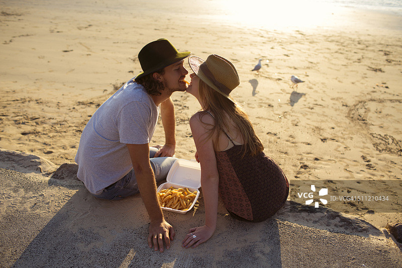 在澳大利亚海滩日落时分互相喂薯条的时髦情侣图片素材