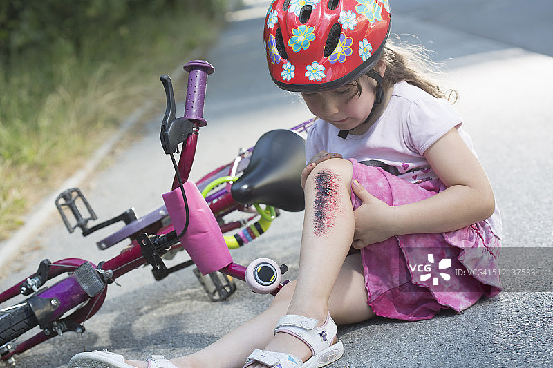 受伤的年轻女孩坐在路边，旁边是自行车图片素材
