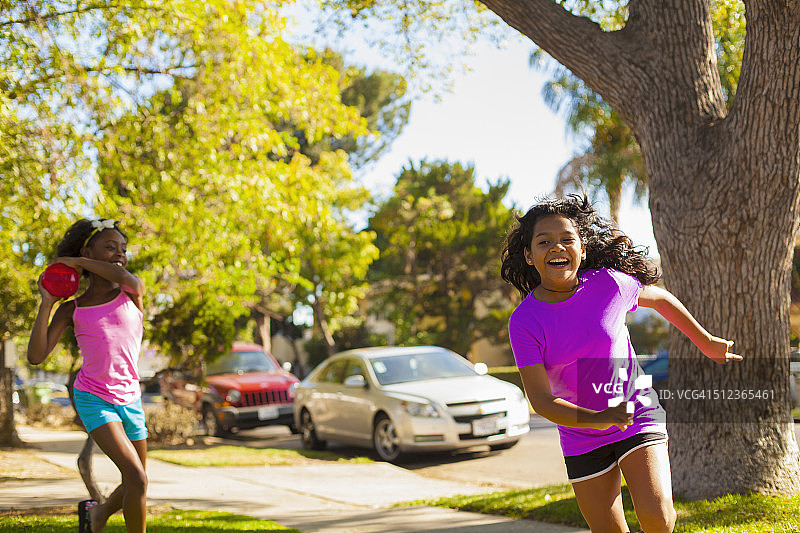 女孩在街上用水气球追逐朋友图片素材