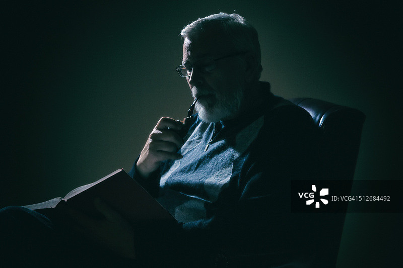 年长的男人在光线昏暗的房间里看书图片素材