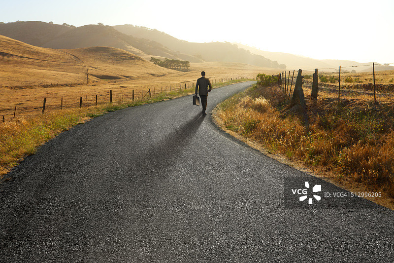 走在弯曲的乡村道路上的商人图片素材