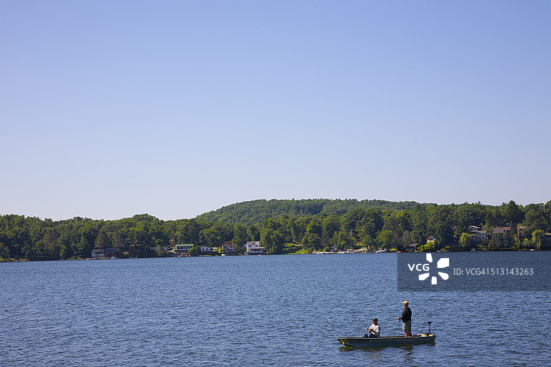 在平静的湖面上从船上钓鱼的男人图片素材