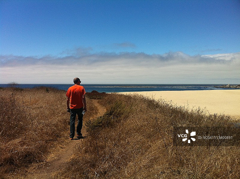 穿着橙色T恤走在小路上的男人图片素材