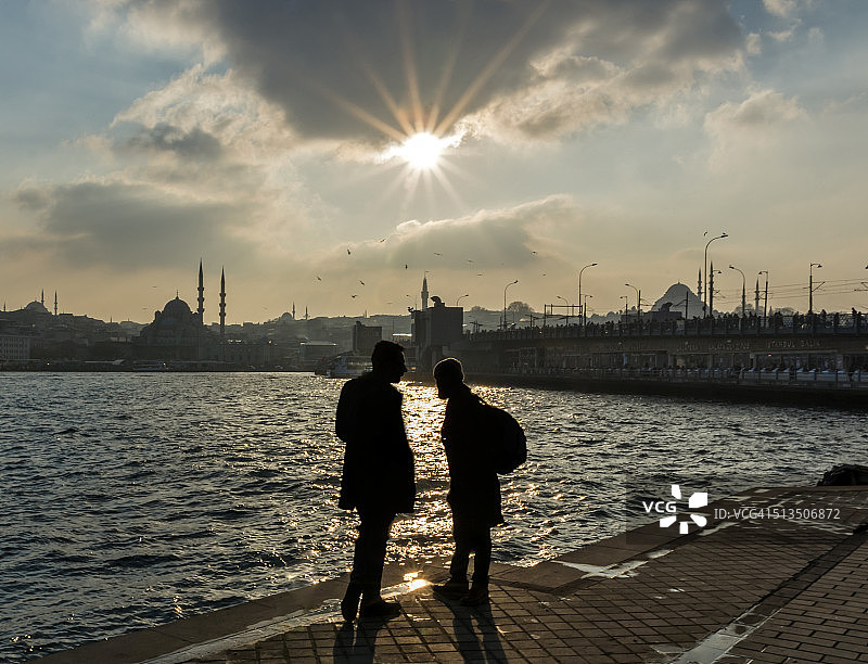 土耳其伊斯坦布尔，两人在日落时分眺望加拉塔大桥和耶尼贾米清真寺的剪影图片素材