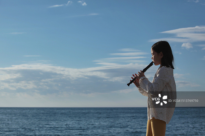 在海滩边自信地吹着竖笛的年轻女孩图片素材