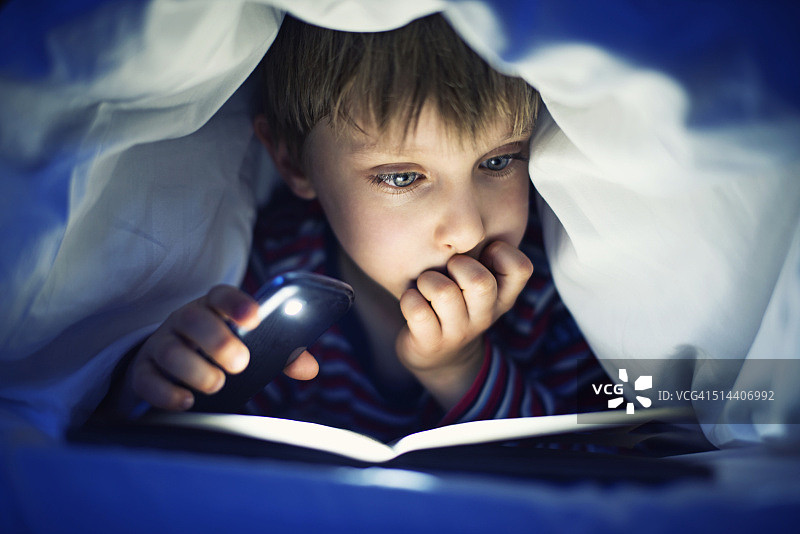 小男孩偷偷地在被窝里看书图片素材