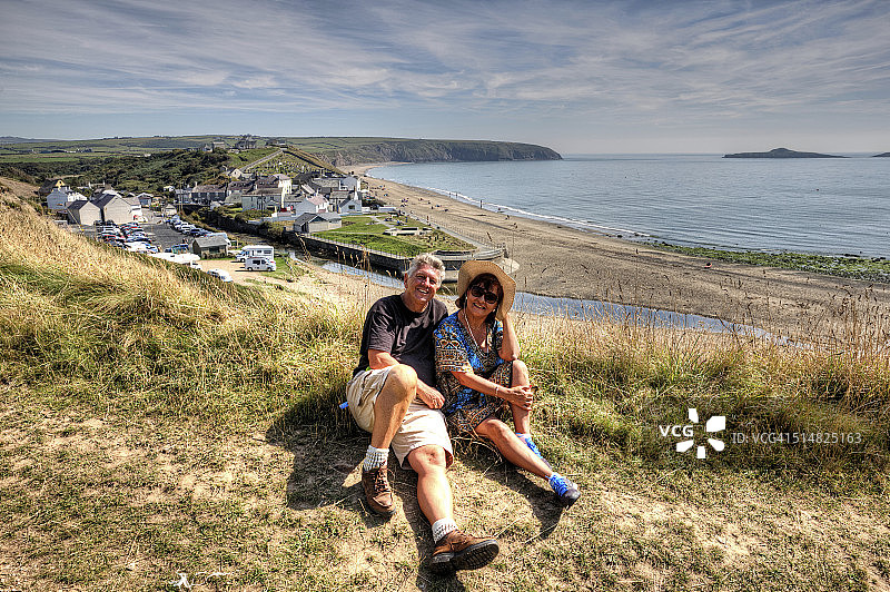 坐在草地上俯瞰海滩的成熟微笑夫妇图片素材