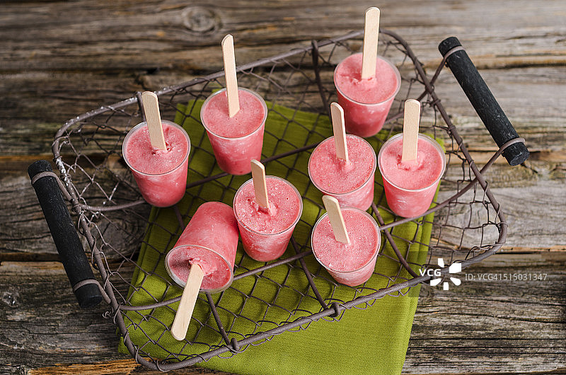 装满自制草莓冰棒的金属丝篮子，置于布和木头上图片素材