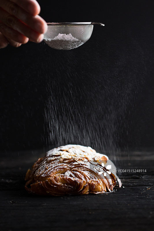 在巧克力羊角面包上撒糖粉图片素材