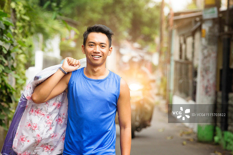 快乐的年轻印度尼西亚男子拿着干洗的衣服图片素材