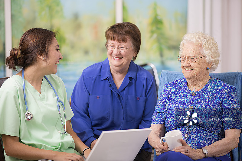 女医生在疗养院拜访老年女病人，使用笔记本电脑图片素材