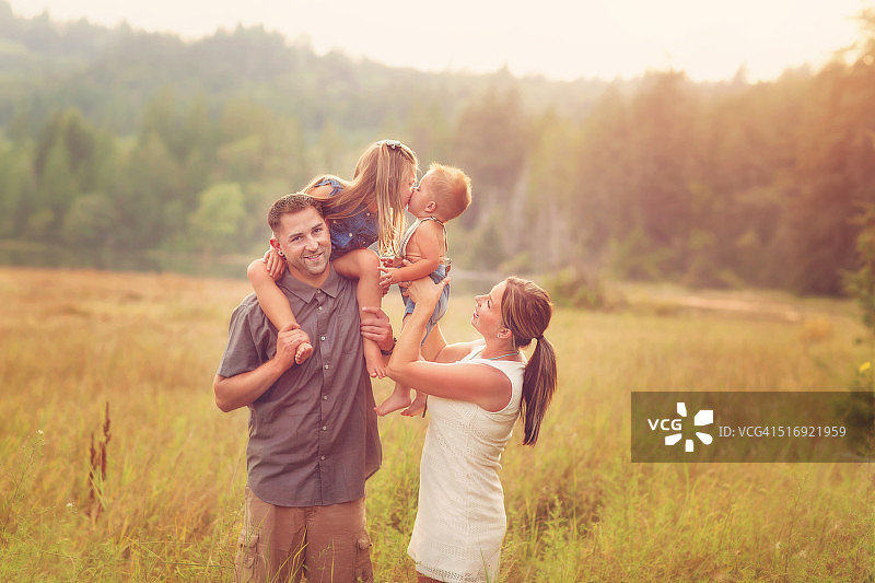 母亲抱起幼儿亲吻他的兄弟姐妹图片素材