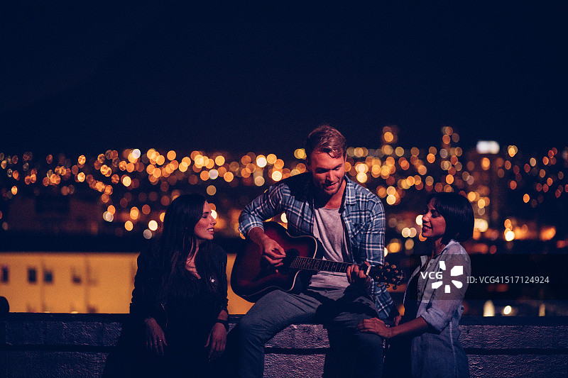 在屋顶为两个朋友弹吉他的年轻男人图片素材