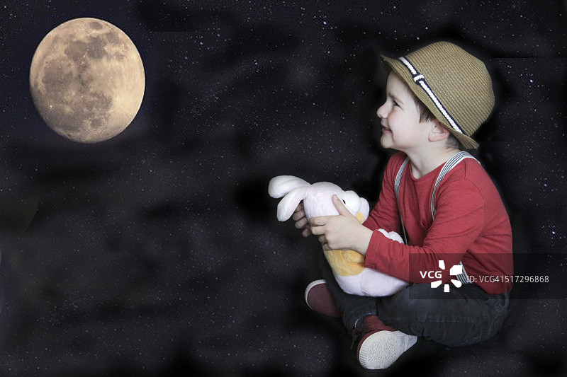 抱着兔子玩具看满月的男孩图片素材