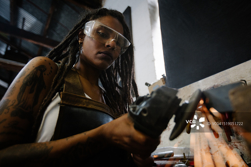 熟练的女工匠戴着安全护目镜使用砂轮机图片素材