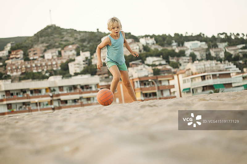 男孩在城市沙滩踢足球图片素材