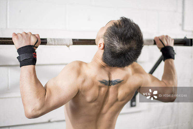 一名男子正在健身房的单杠上做引体向上图片素材