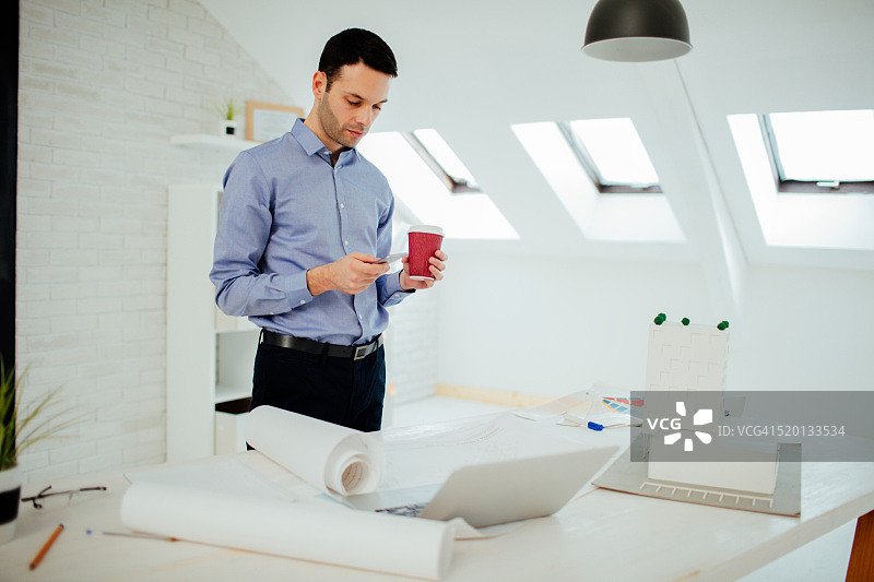 建筑师在办公室喝咖啡和使用智能手机图片素材