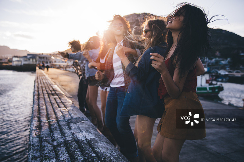 在日落时分码头上跳舞的青少年朋友图片素材