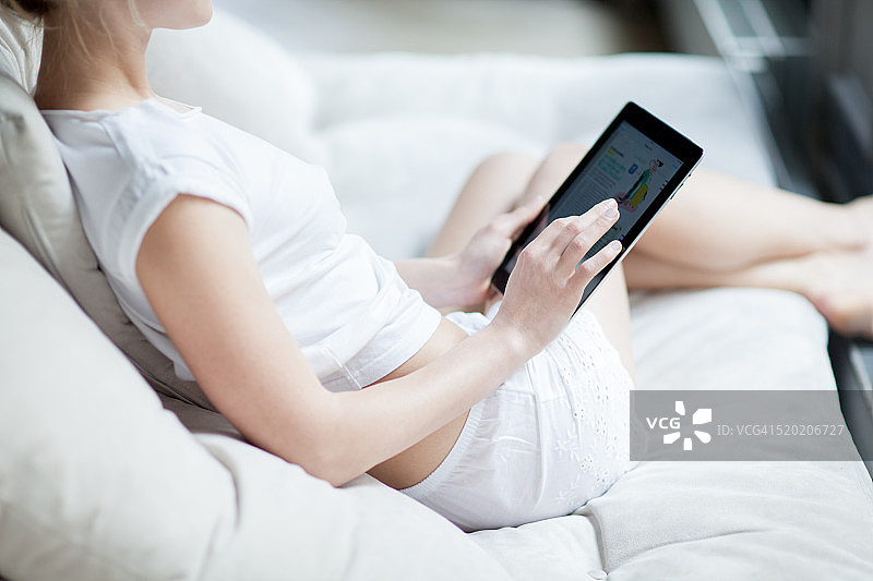 穿着内衣坐在沙发上使用平板电脑的女人图片素材