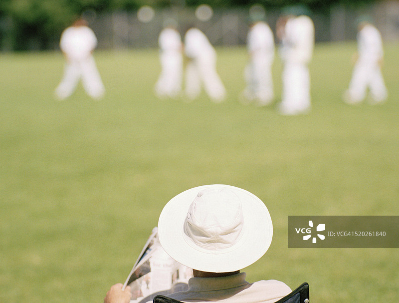 戴着白色帽子和拿着报纸观看板球比赛的男人图片素材