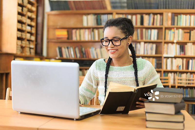 微笑的高中生在图书馆使用笔记本电脑图片素材
