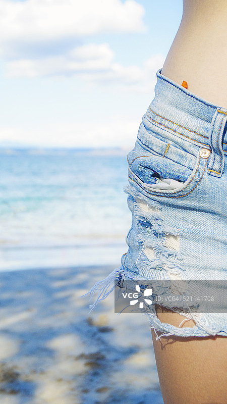 海滩上穿着蓝色牛仔短裤的女人的臀部的竖版照片图片素材
