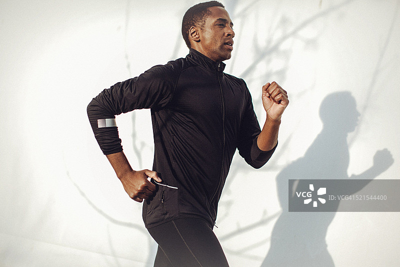 年轻健壮的男人在白墙边跑步图片素材