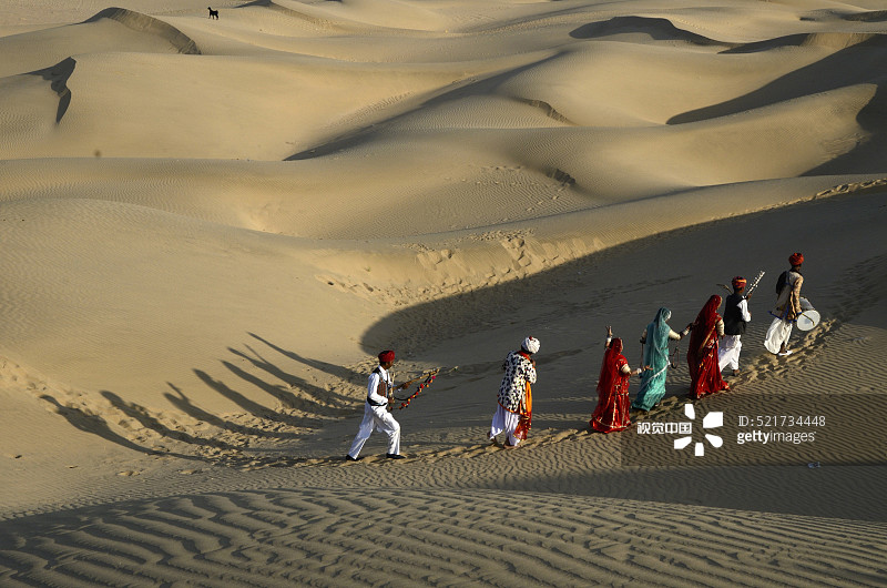 在印度拉贾斯坦邦斋沙默尔的沙丘上行走的民间音乐家和舞者图片素材