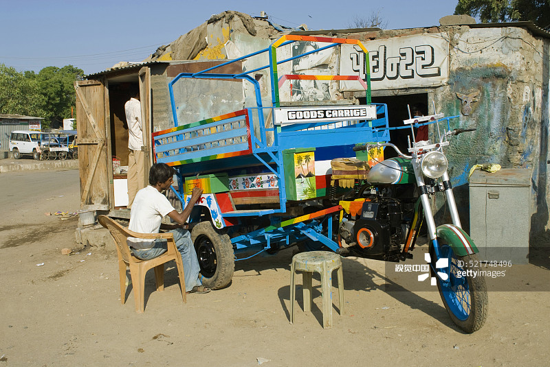 印度古吉拉特邦安贾尔的路边画家正在给连接摩托车的货物车上漆图片素材