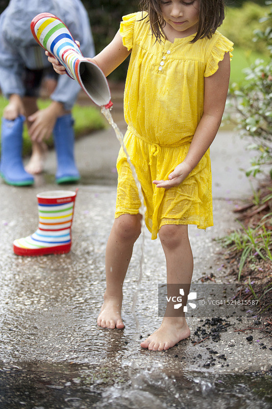 女孩将雨靴里的水倒入水坑图片素材